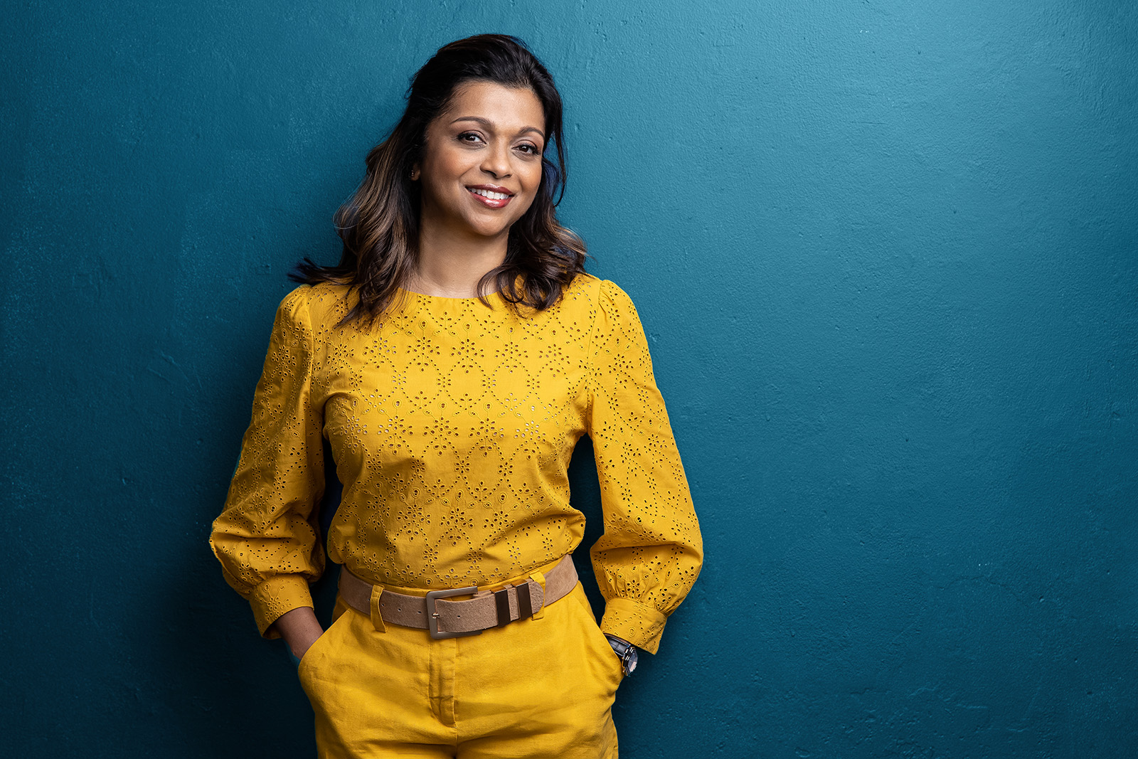 professional headshot Indian lady standing on a teal wall in yellow clothing for a headshot